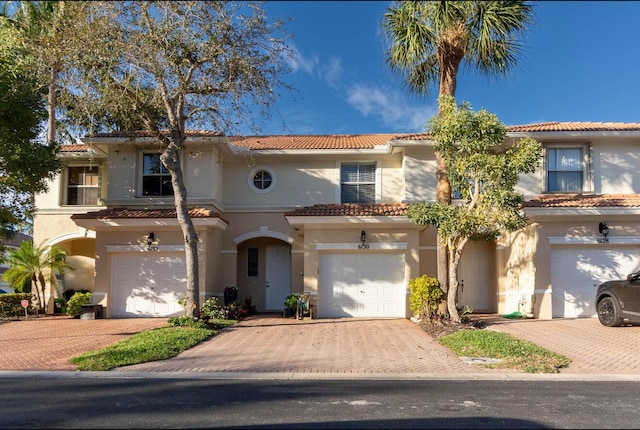 mediterranean / spanish-style home with a garage, a tiled roof, decorative driveway, and stucco siding