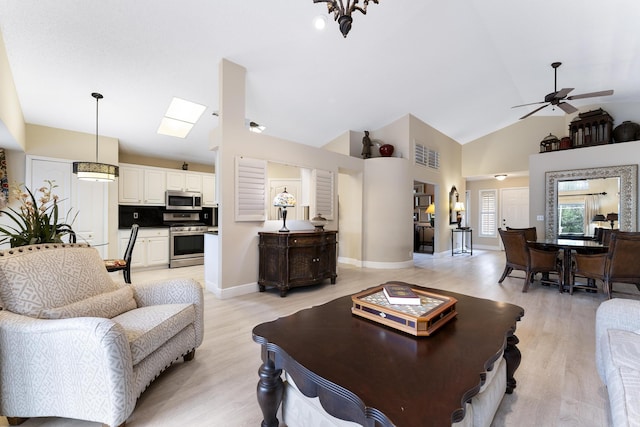 living area with baseboards, high vaulted ceiling, light wood-style flooring, and a ceiling fan