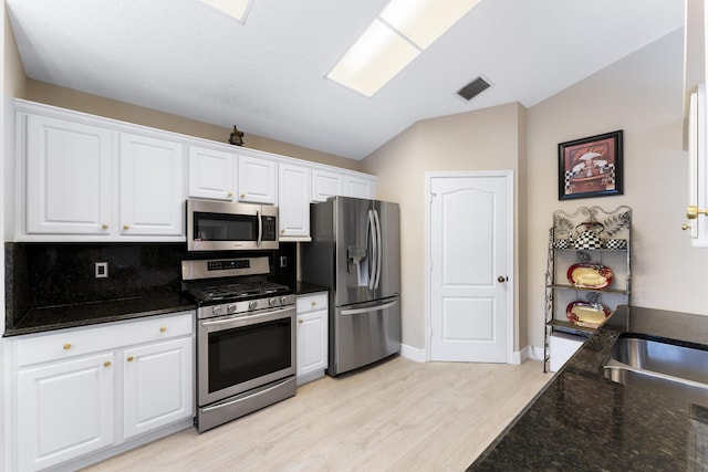 kitchen with lofted ceiling, stainless steel appliances, visible vents, and white cabinets