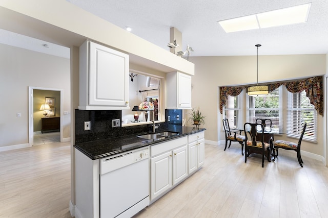 kitchen featuring tasteful backsplash, white cabinets, a sink, vaulted ceiling with skylight, and dishwasher