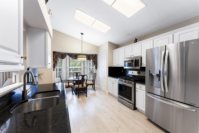 kitchen featuring stainless steel appliances, light wood-style floors, white cabinets, a sink, and vaulted ceiling with skylight