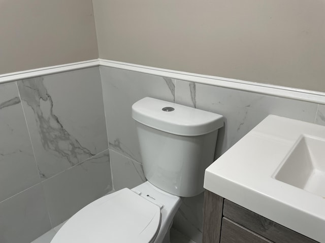 half bath featuring wainscoting, a sink, tile walls, and toilet