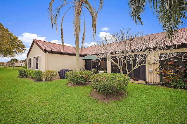 rear view of house featuring a tiled roof, a lawn, and stucco siding