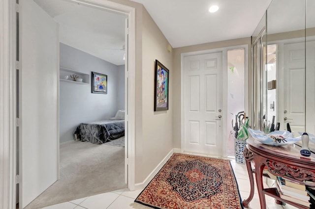 foyer entrance featuring a ceiling fan, light colored carpet, light tile patterned flooring, and baseboards