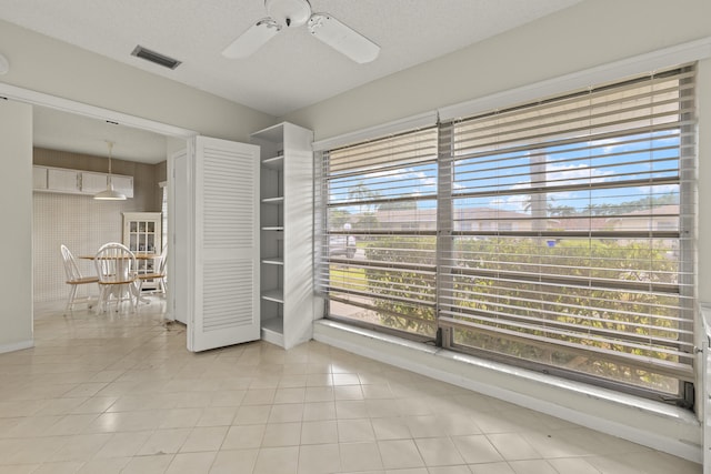 empty room featuring light tile patterned floors, ceiling fan, visible vents, and a textured ceiling