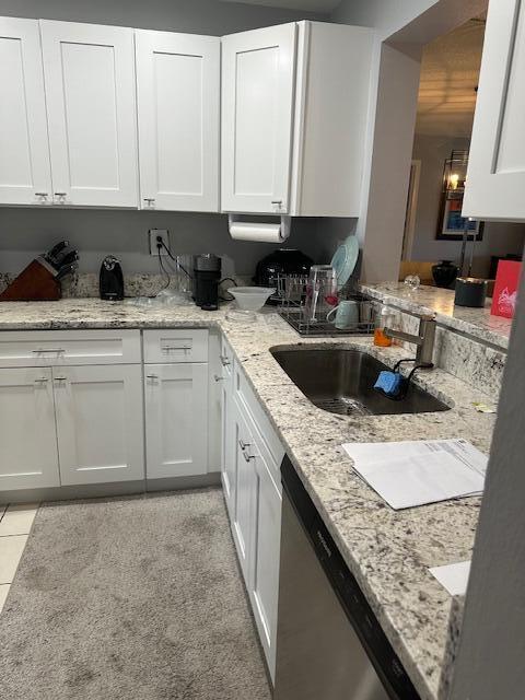 kitchen with light stone counters, white cabinetry, dishwasher, and a sink