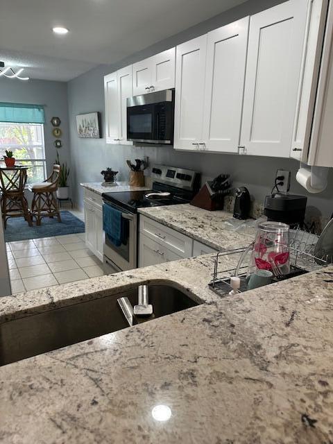 kitchen with electric range, light stone counters, light tile patterned flooring, white cabinetry, and recessed lighting