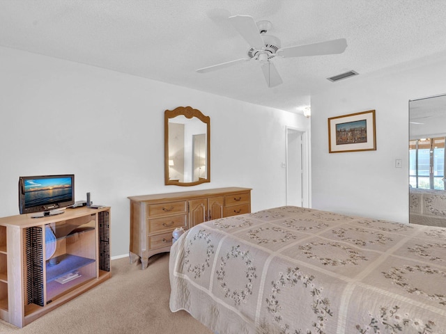 bedroom featuring ceiling fan, visible vents, a textured ceiling, and light colored carpet