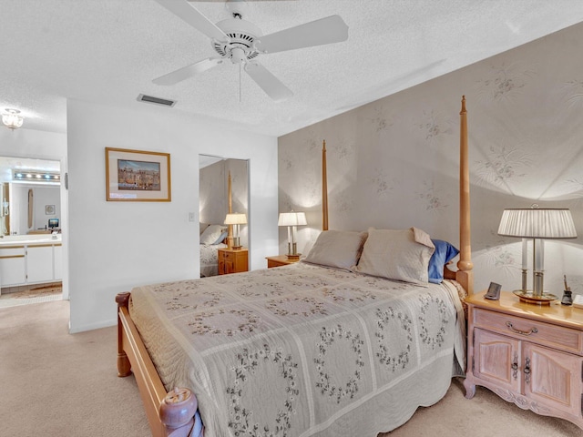 bedroom featuring a textured ceiling, connected bathroom, light colored carpet, a ceiling fan, and visible vents