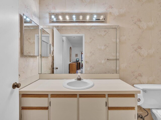 bathroom with toilet, vanity, and wallpapered walls