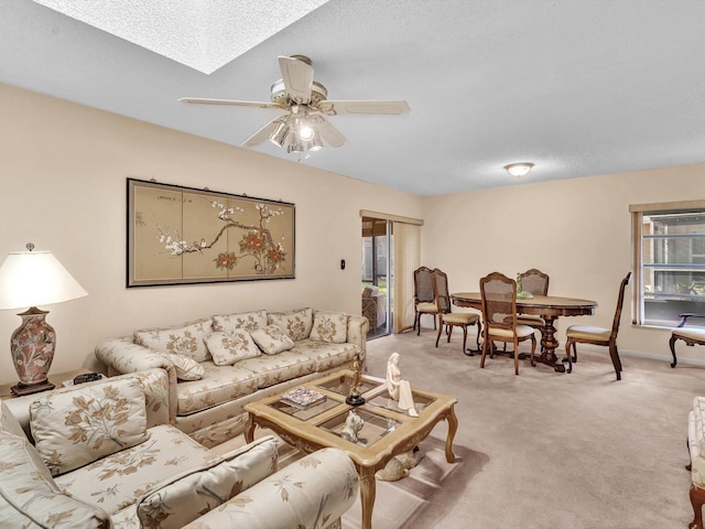 living room featuring a skylight, baseboards, light colored carpet, ceiling fan, and a textured ceiling