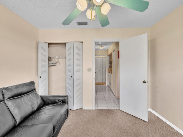 living area featuring a textured ceiling, light colored carpet, a ceiling fan, baseboards, and visible vents