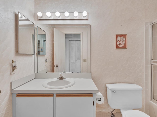 bathroom with combined bath / shower with glass door, vanity, toilet, and wallpapered walls