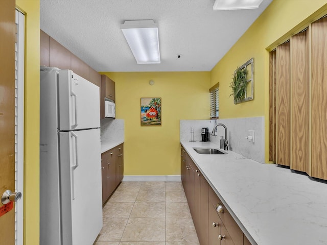 kitchen with light tile patterned floors, a textured ceiling, white appliances, a sink, and tasteful backsplash