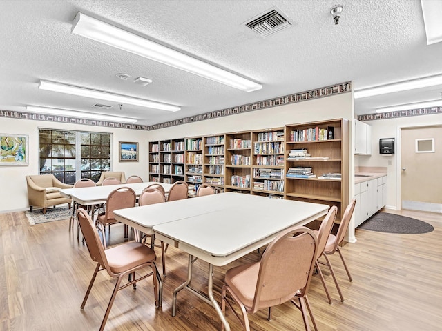 dining area with a textured ceiling, light wood-type flooring, and visible vents