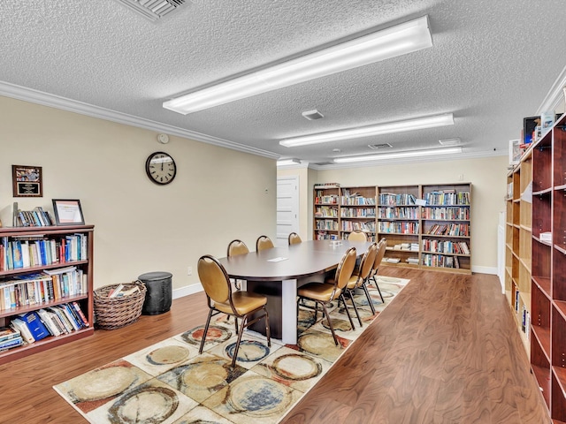 dining room featuring a textured ceiling, baseboards, wood finished floors, and crown molding