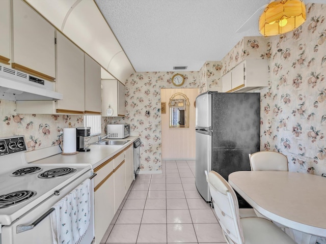 kitchen with a textured ceiling, light tile patterned floors, under cabinet range hood, stainless steel appliances, and wallpapered walls