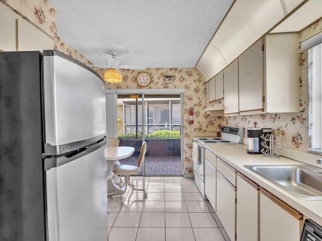 kitchen featuring white electric stove, under cabinet range hood, light countertops, freestanding refrigerator, and wallpapered walls