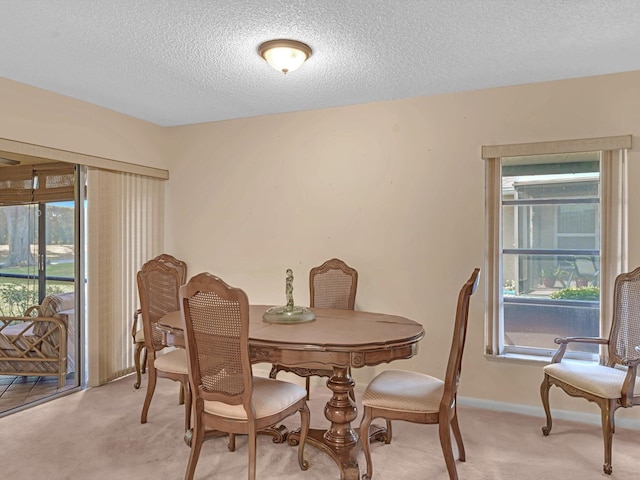 dining room with a healthy amount of sunlight, light carpet, baseboards, and a textured ceiling