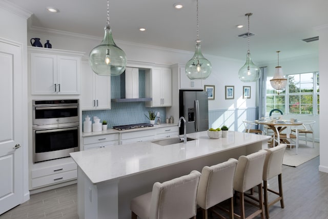 kitchen with stainless steel appliances, a sink, ornamental molding, wall chimney range hood, and a kitchen bar