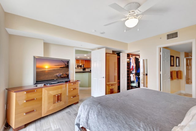 bedroom featuring visible vents, baseboards, ensuite bath, light wood-style flooring, and a walk in closet