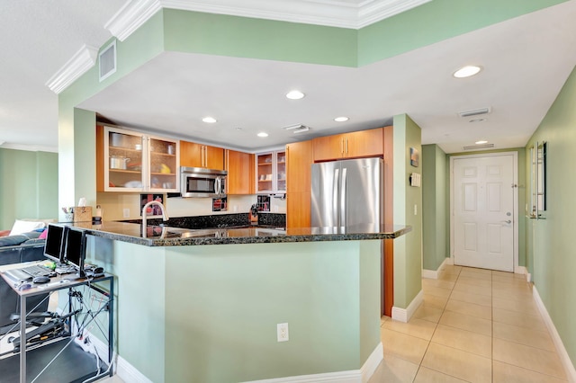 kitchen with stainless steel appliances, a peninsula, ornamental molding, dark stone countertops, and glass insert cabinets