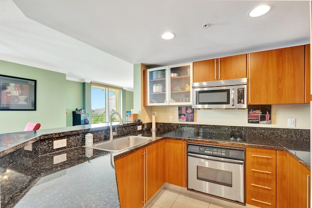 kitchen with glass insert cabinets, appliances with stainless steel finishes, dark stone counters, and a sink