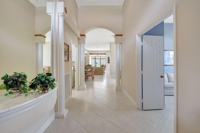 hallway with baseboards, arched walkways, a high ceiling, ornate columns, and light tile patterned flooring