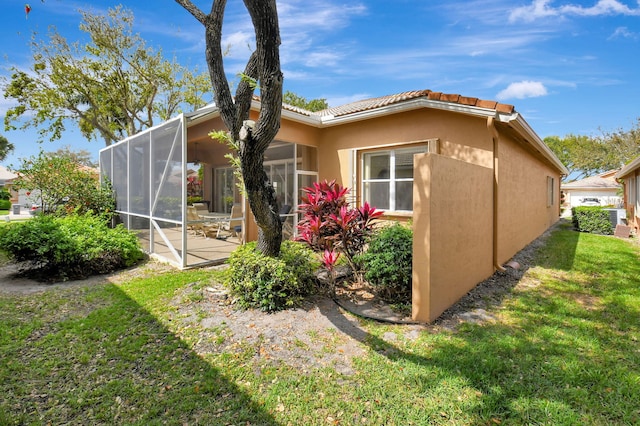 view of home's exterior with glass enclosure, a tiled roof, a yard, a patio area, and stucco siding