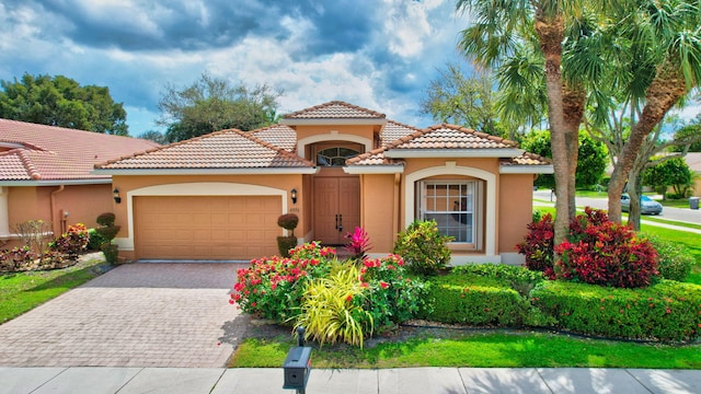 mediterranean / spanish-style home featuring a garage, decorative driveway, a tile roof, and stucco siding