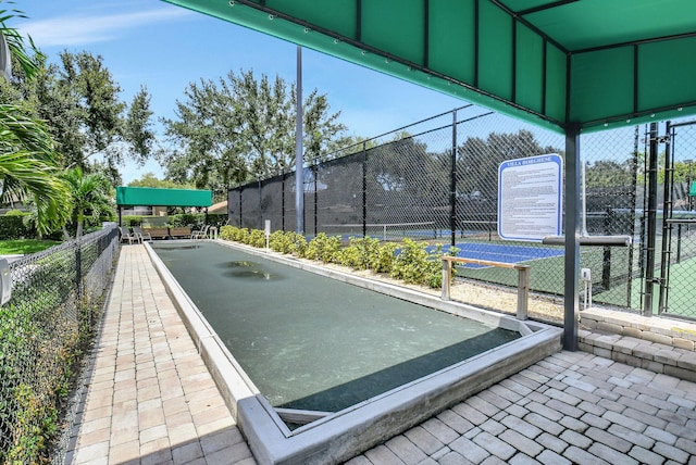 view of community featuring a tennis court, a gate, and fence