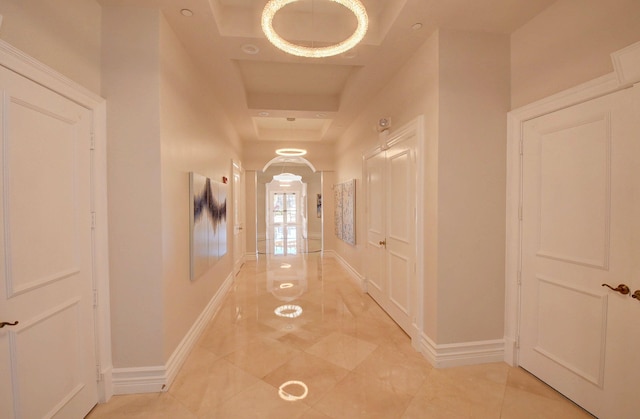 hallway featuring baseboards, arched walkways, and a raised ceiling