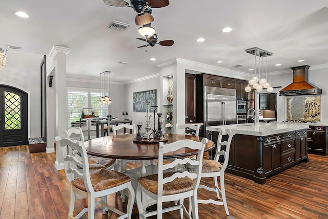 dining space with dark wood-type flooring, visible vents, ornamental molding, and ceiling fan with notable chandelier