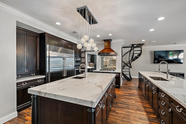 kitchen featuring a center island with sink, custom exhaust hood, appliances with stainless steel finishes, dark wood-type flooring, and a sink