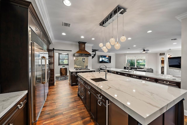 kitchen with a barn door, visible vents, appliances with stainless steel finishes, premium range hood, and a sink