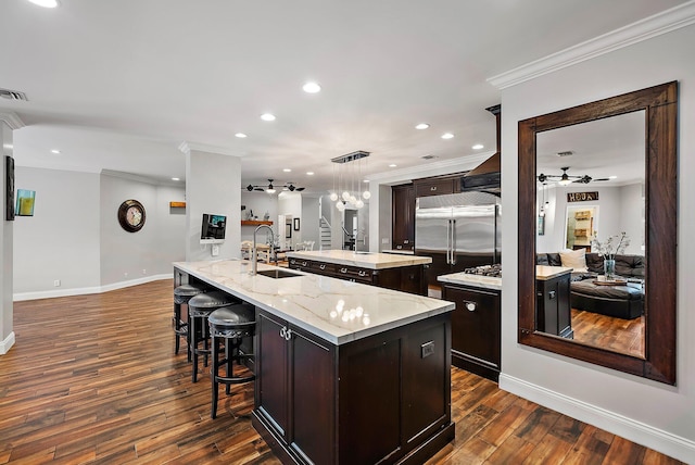 kitchen featuring built in fridge, dark wood-type flooring, ornamental molding, a sink, and an island with sink