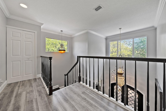 staircase featuring a textured ceiling, wood finished floors, visible vents, baseboards, and crown molding