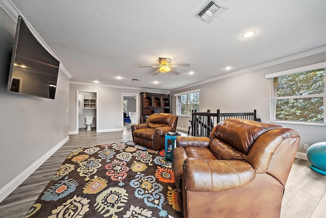 living area with a textured ceiling, visible vents, crown molding, and wood finished floors