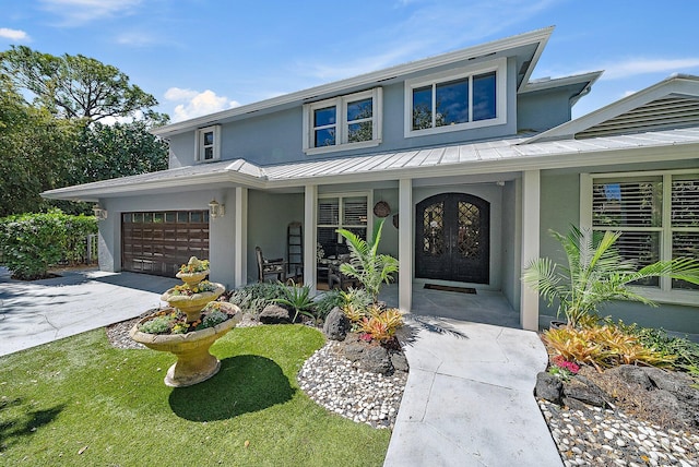 view of front of home with french doors, stucco siding, a porch, a standing seam roof, and a garage