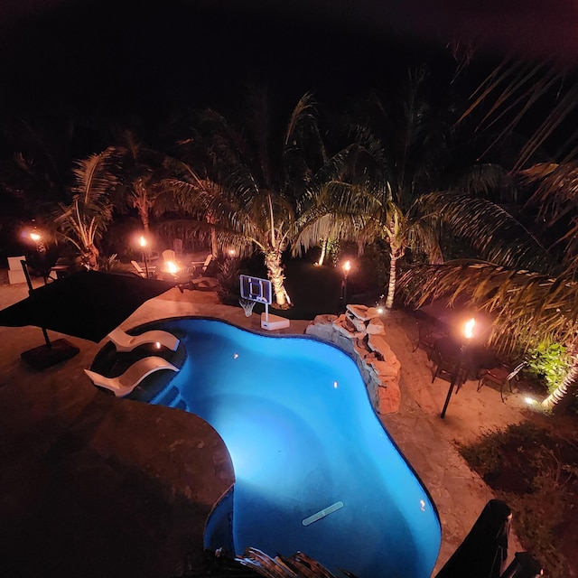 pool at night with an outdoor pool and a patio