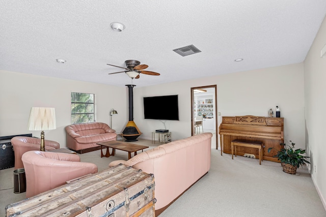 living room featuring light carpet, visible vents, ceiling fan, a wood stove, and a textured ceiling