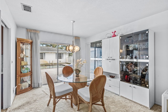 dining room featuring an inviting chandelier, visible vents, a textured ceiling, and light colored carpet