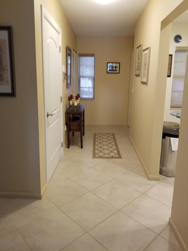 hall with a textured ceiling, baseboards, and light tile patterned floors