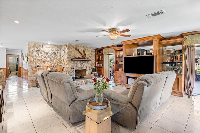 living room with light tile patterned floors, ceiling fan, a stone fireplace, and visible vents