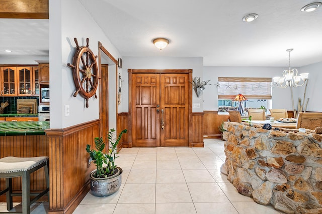 foyer entrance with light tile patterned floors, a wainscoted wall, a notable chandelier, wooden walls, and recessed lighting