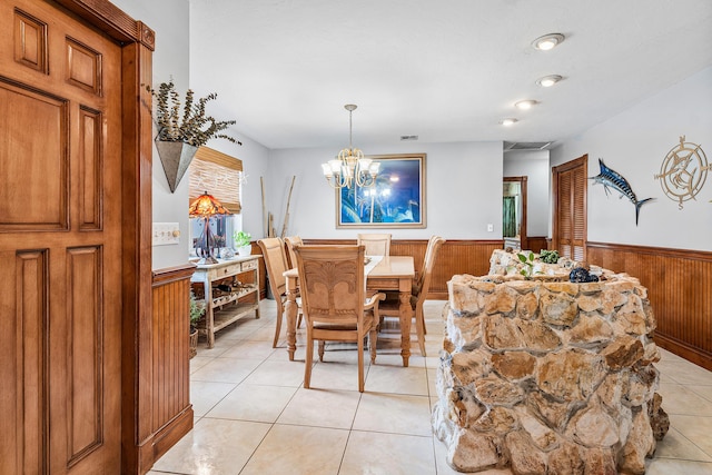 dining room with light tile patterned floors, a notable chandelier, wood walls, and a wainscoted wall