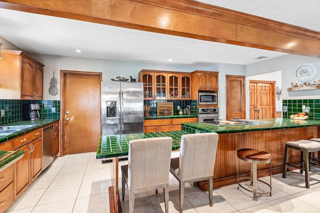 kitchen with tile countertops, stainless steel appliances, decorative backsplash, and a breakfast bar area