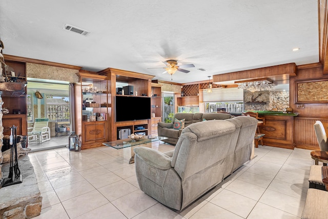 living room with ceiling fan, wood walls, light tile patterned flooring, and visible vents