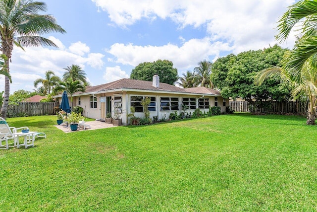 rear view of house with a patio area, stucco siding, fence private yard, a chimney, and a lawn
