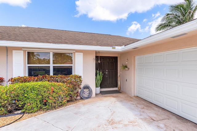 view of exterior entry with concrete driveway, stucco siding, roof with shingles, and a garage